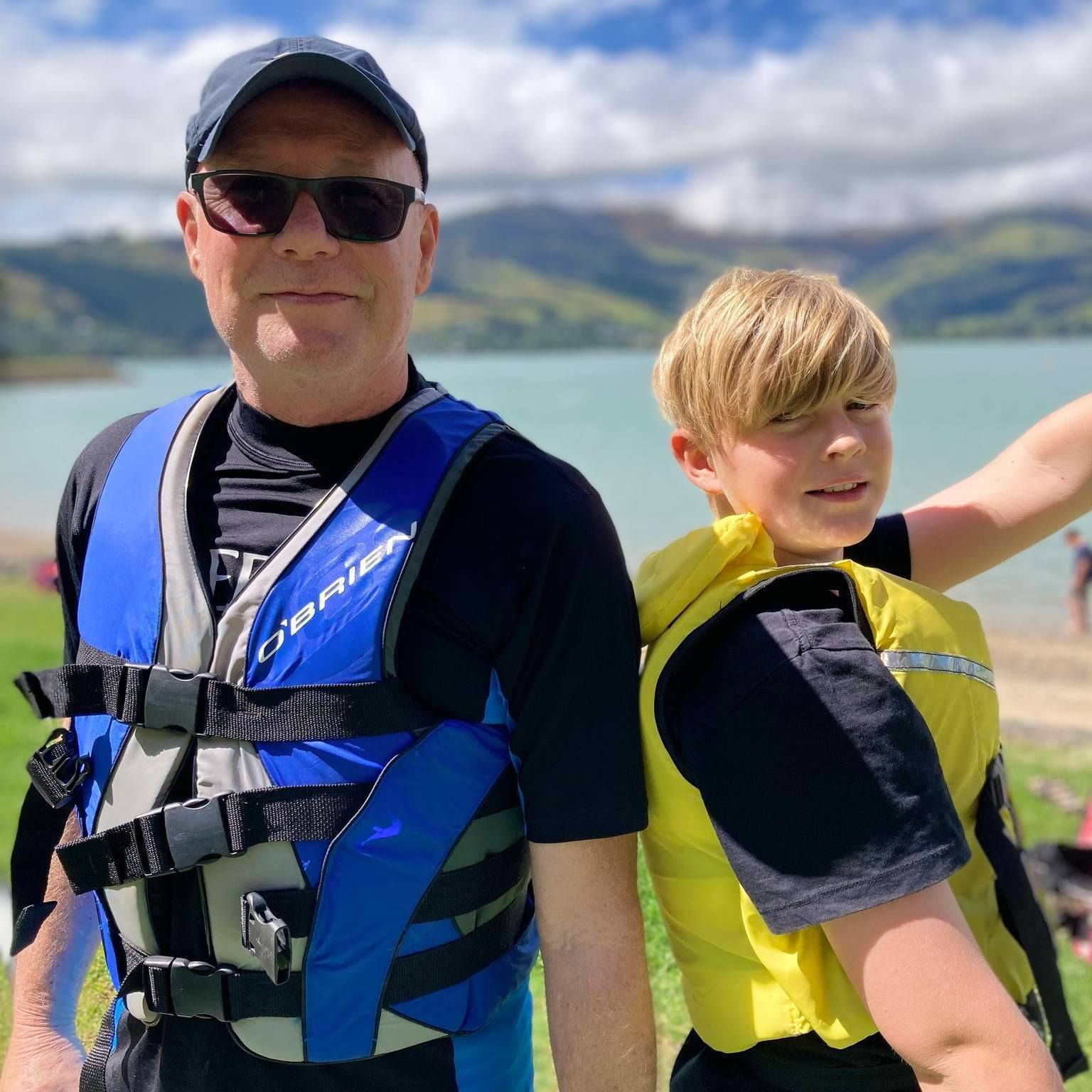 A man and a boy are standing next to each other wearing life jackets.