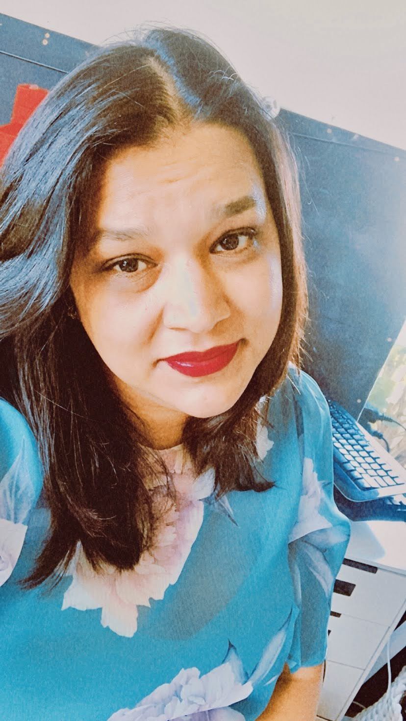 A woman wearing a blue shirt and red lipstick is taking a selfie.