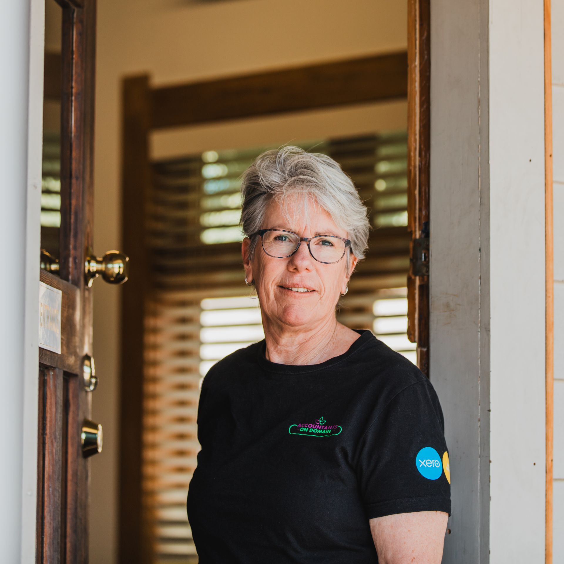 A woman wearing glasses and a black shirt is standing in a doorway.