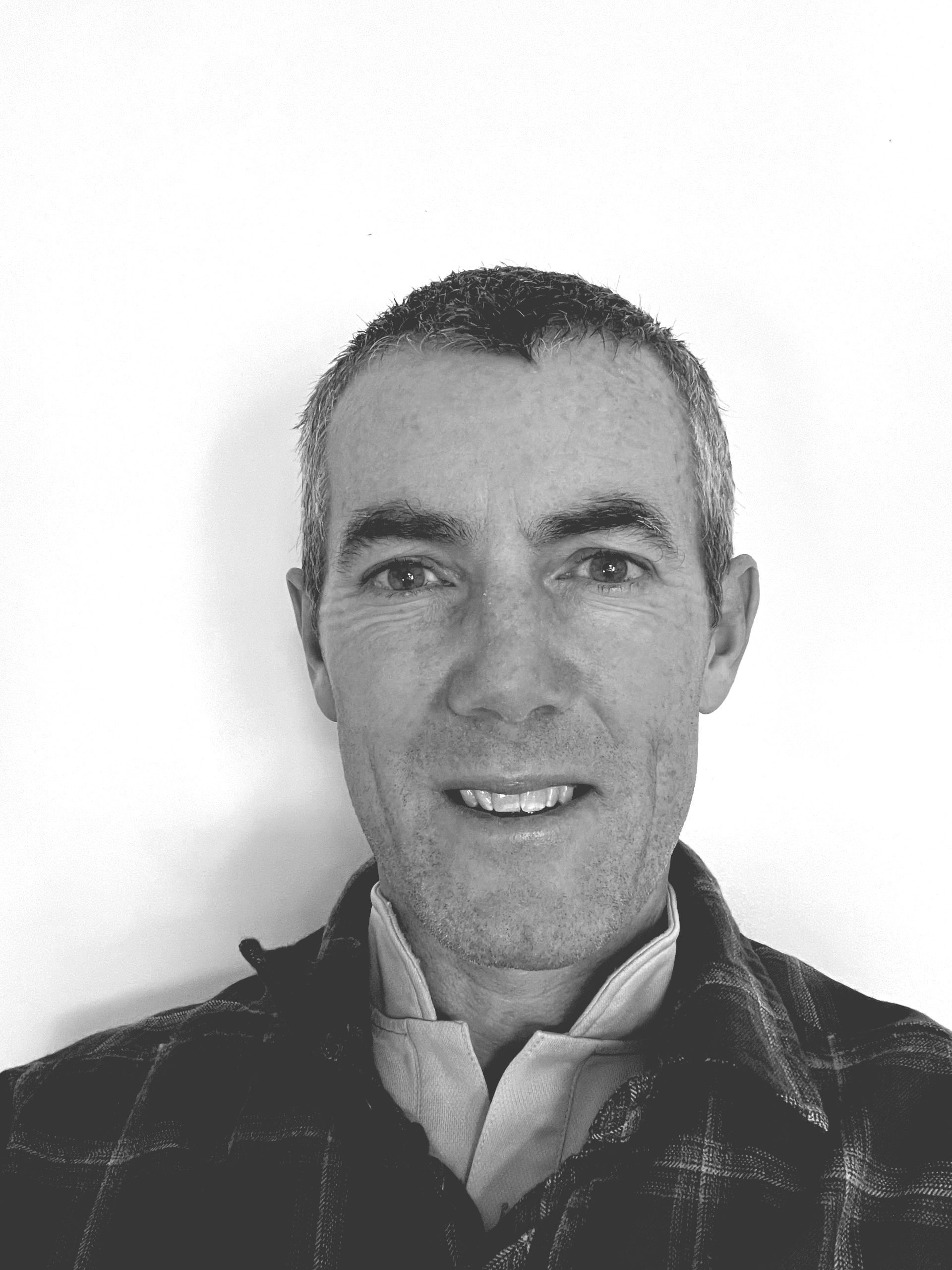 A man in a plaid jacket is smiling in a black and white photo.