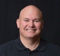A bald man in a black shirt is smiling for the camera.