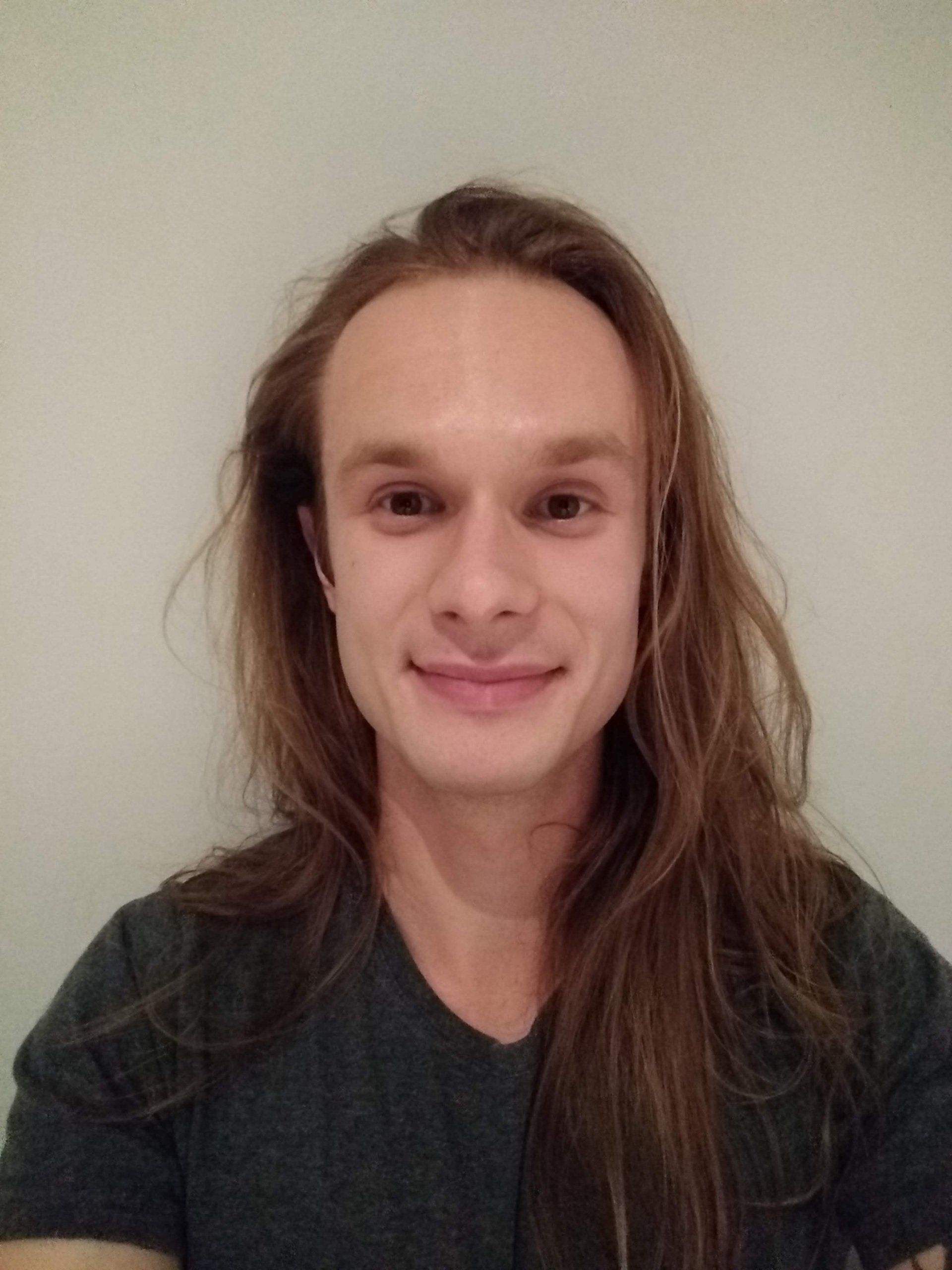 A young man with long hair is smiling for the camera.