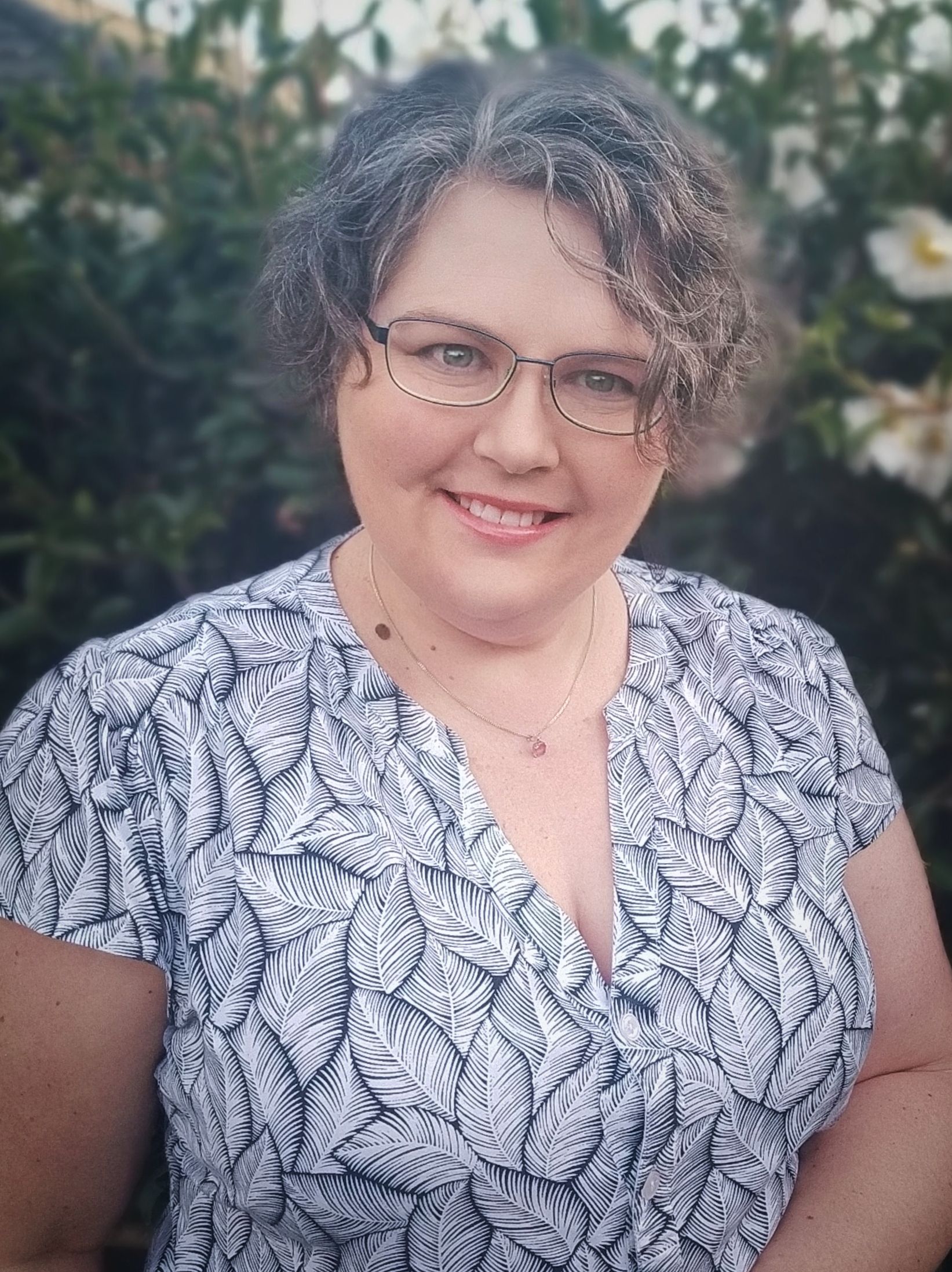 A woman wearing glasses and a floral shirt is smiling for the camera.