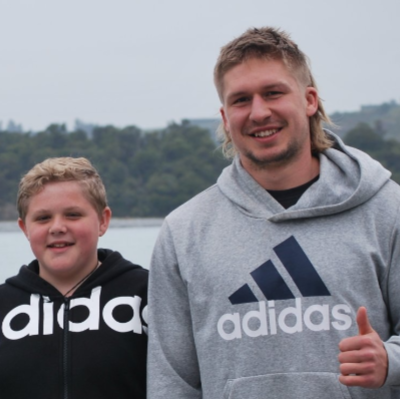 A man wearing an adidas sweatshirt stands next to another man