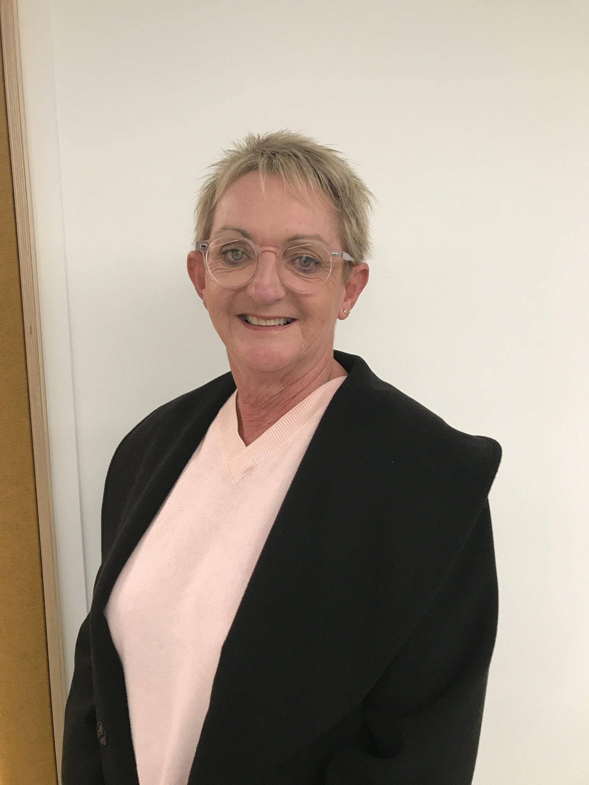 A woman wearing glasses and a black jacket is smiling for the camera.