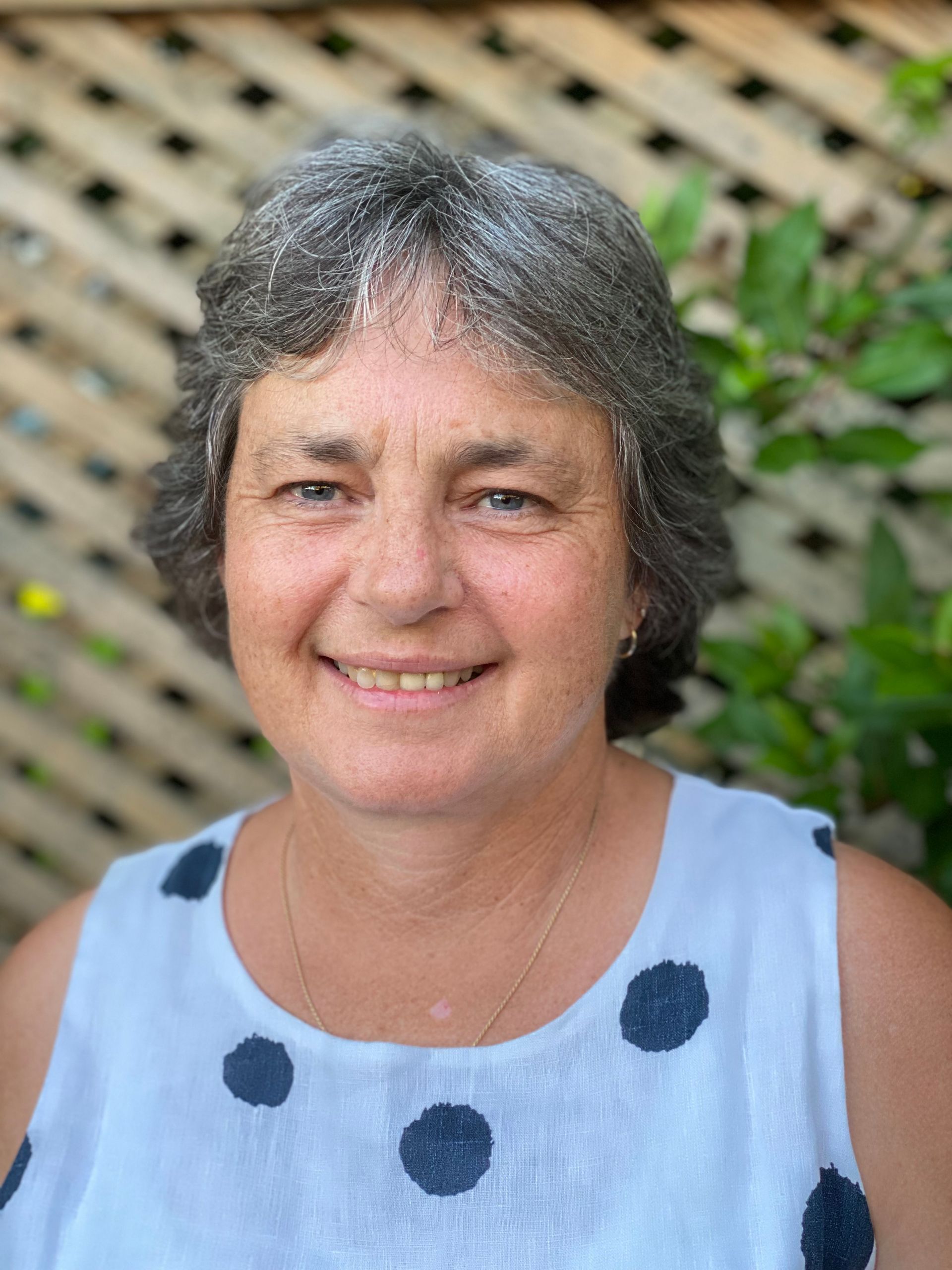 A woman in a white tank top with black polka dots is smiling for the camera.