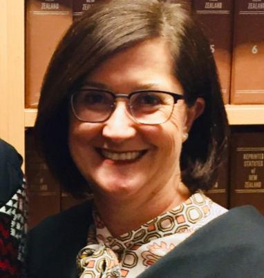 A woman wearing glasses is smiling in front of a bookshelf