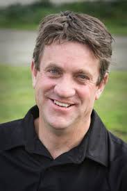 A man in a black shirt is smiling for the camera.
