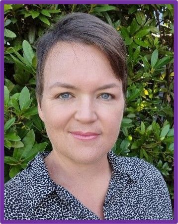 A woman in a black and white shirt is smiling in front of a bush.