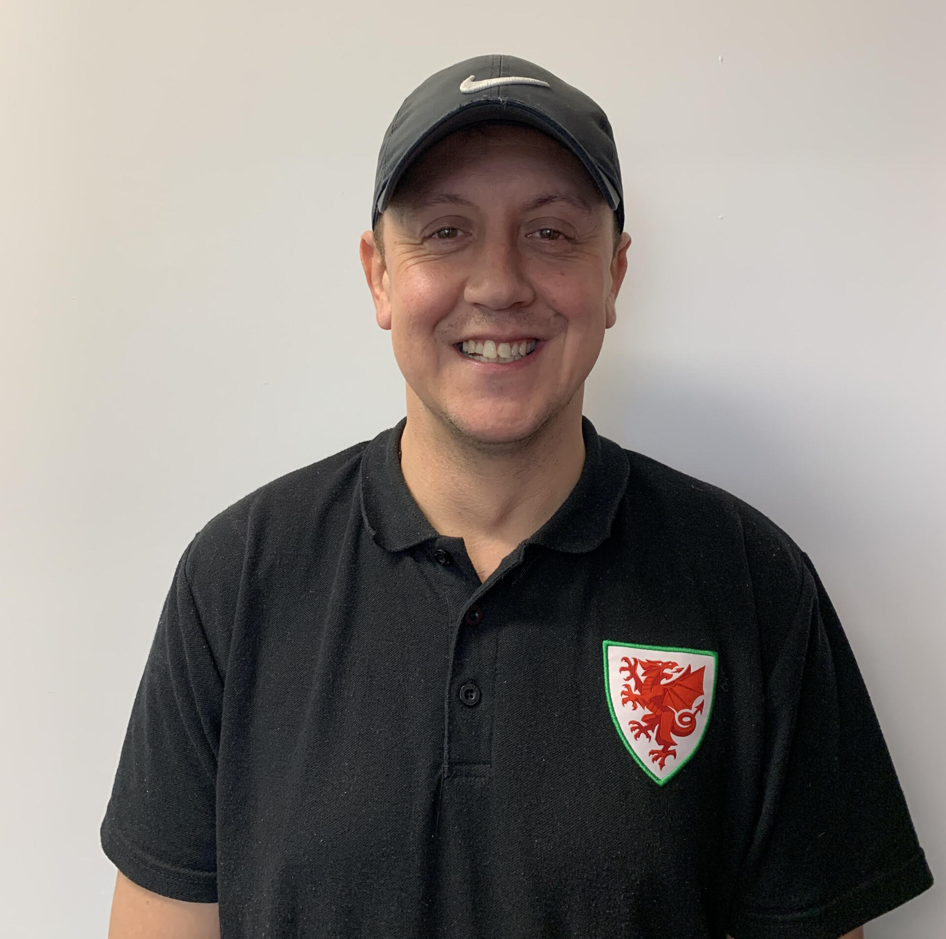 A man wearing a black polo shirt and a hat is smiling for the camera.