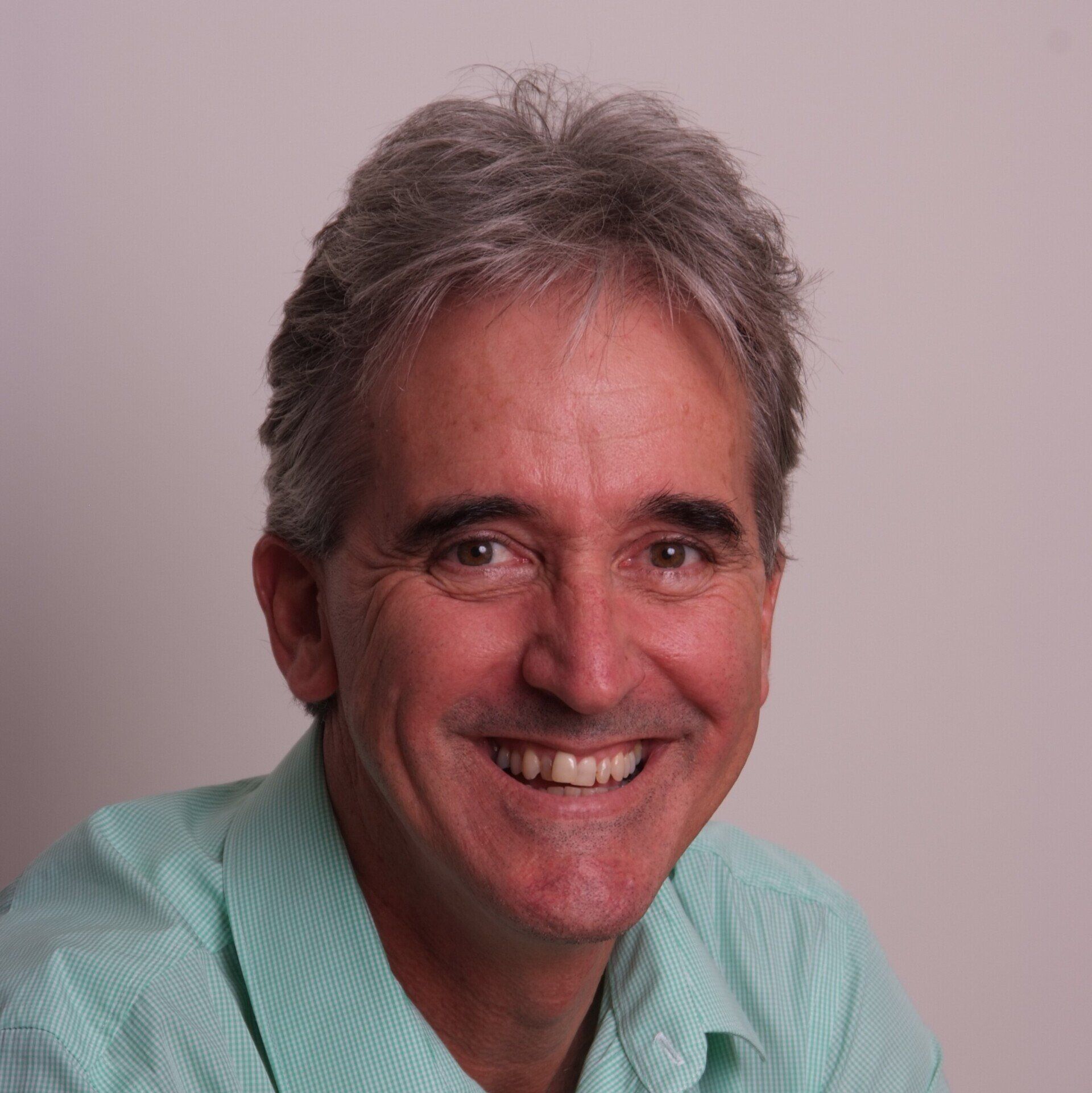 A man with gray hair and a green shirt is smiling for the camera.