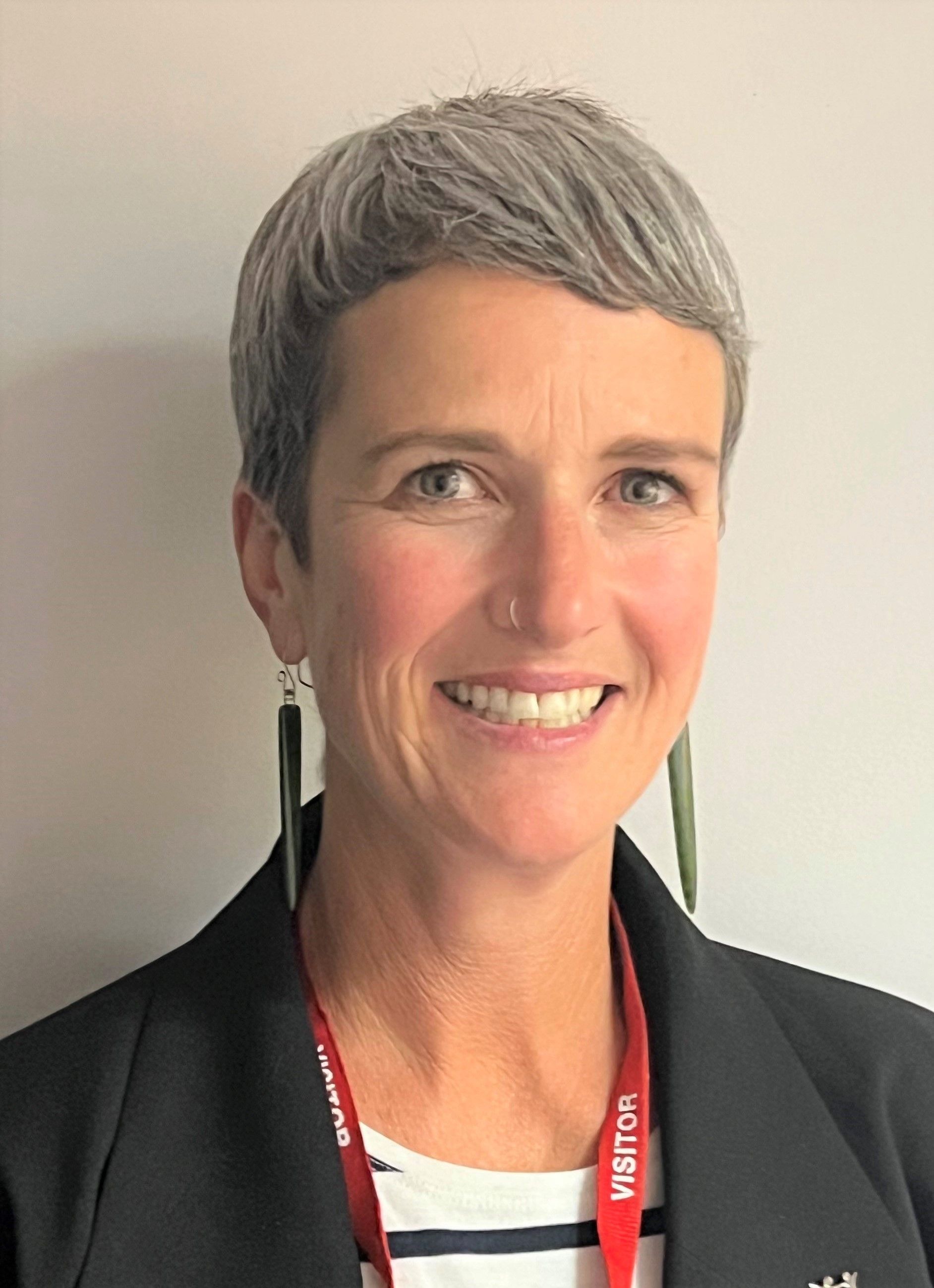 A woman with short gray hair is smiling and wearing a lanyard around her neck.