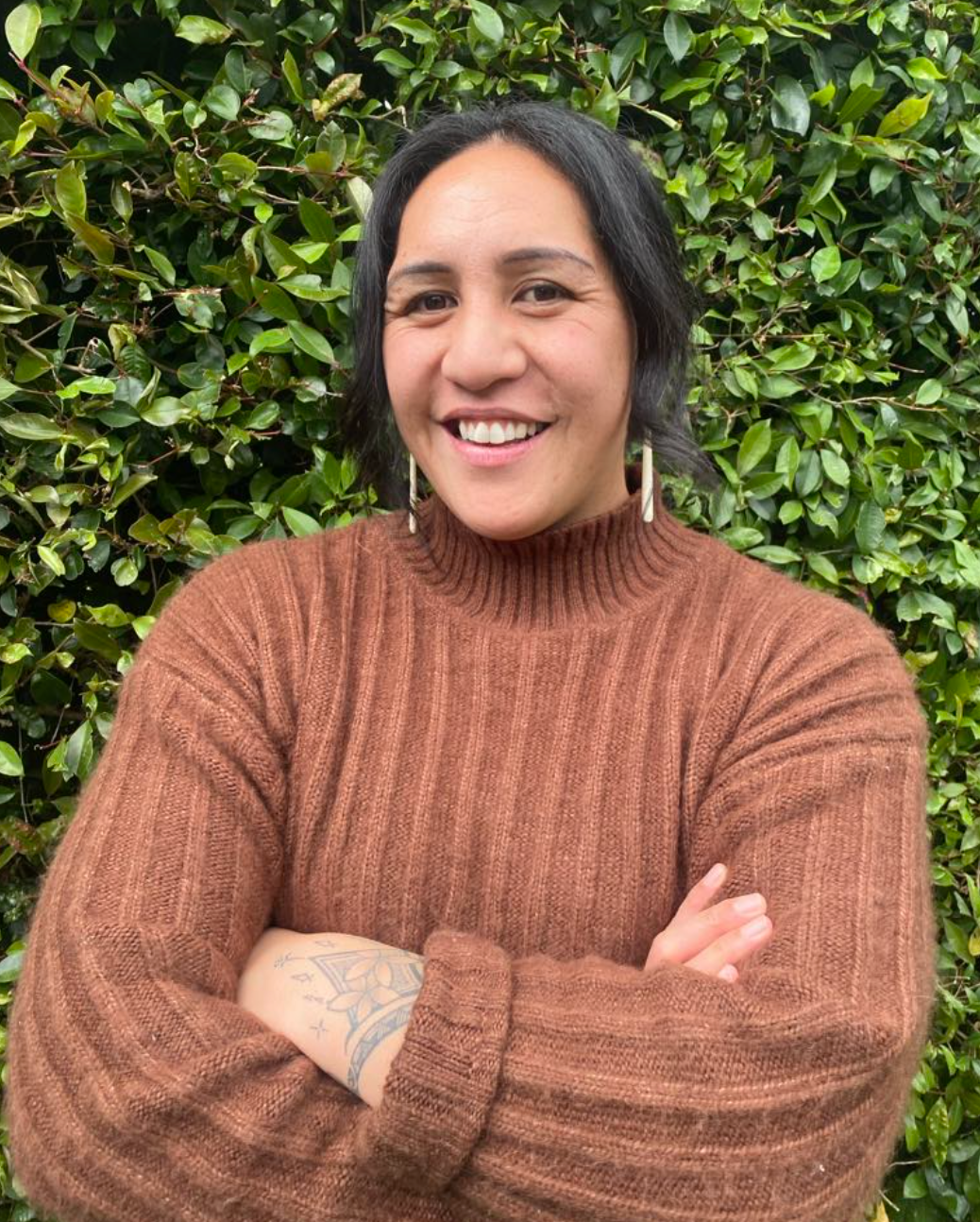 A woman with long curly hair is wearing a black sweater and smiling.