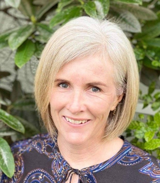 A woman is smiling for the camera in front of a tree.