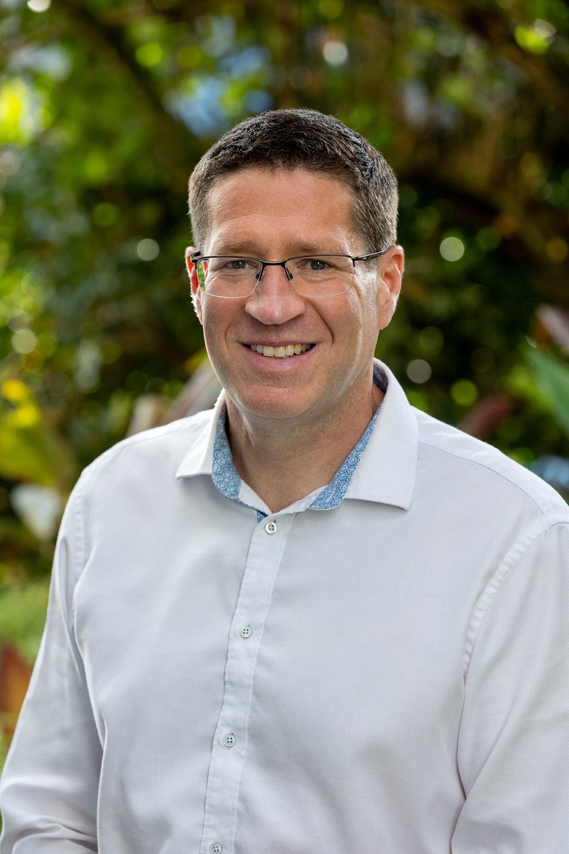A man wearing glasses and a white shirt is smiling for the camera.