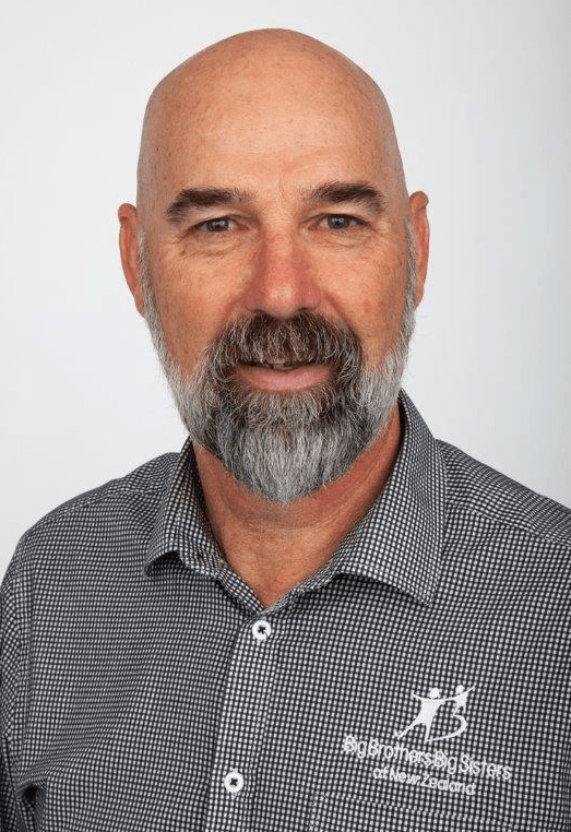 A bald man with a beard is wearing a plaid shirt and smiling.