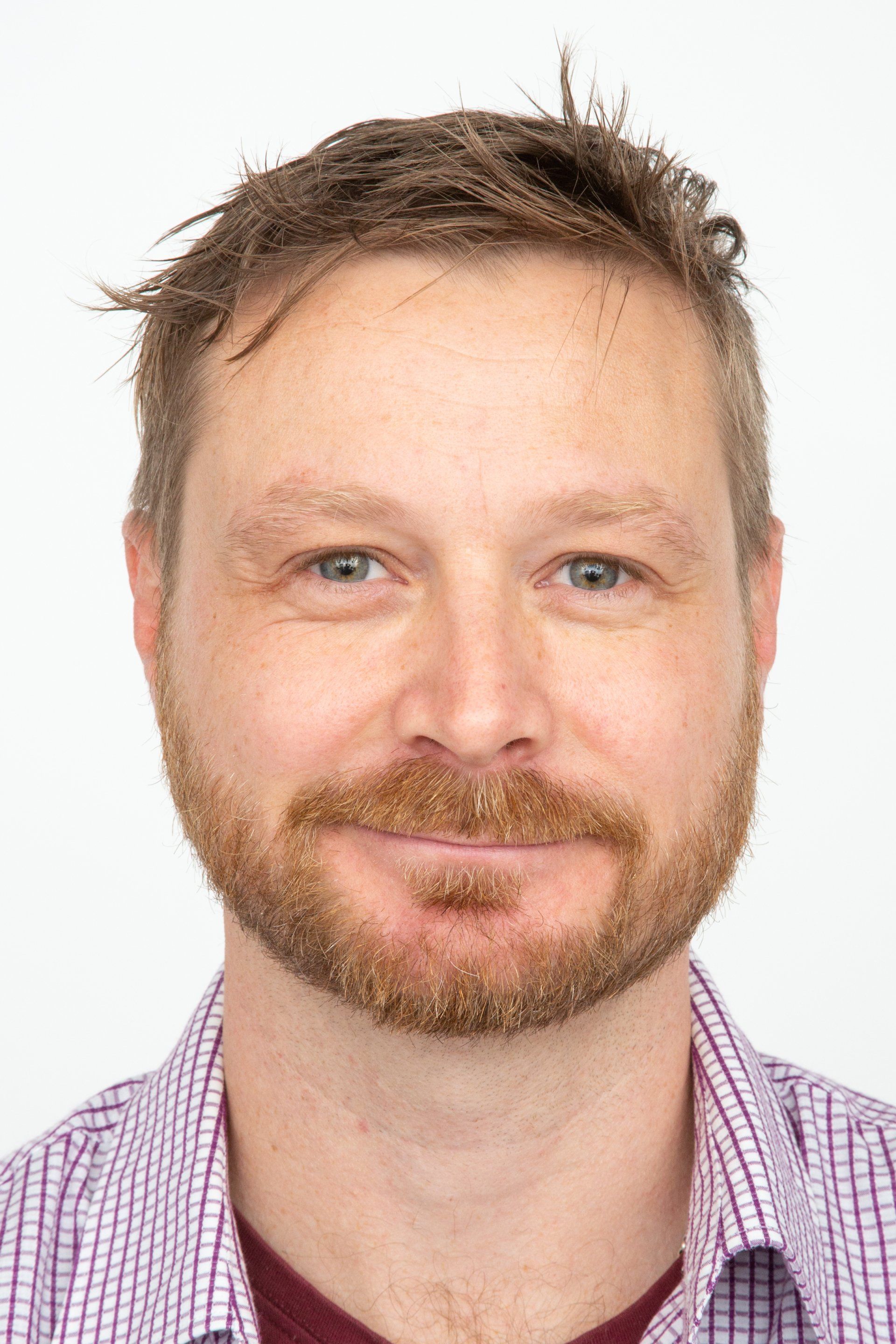 A man with a beard and a plaid shirt is smiling for the camera.