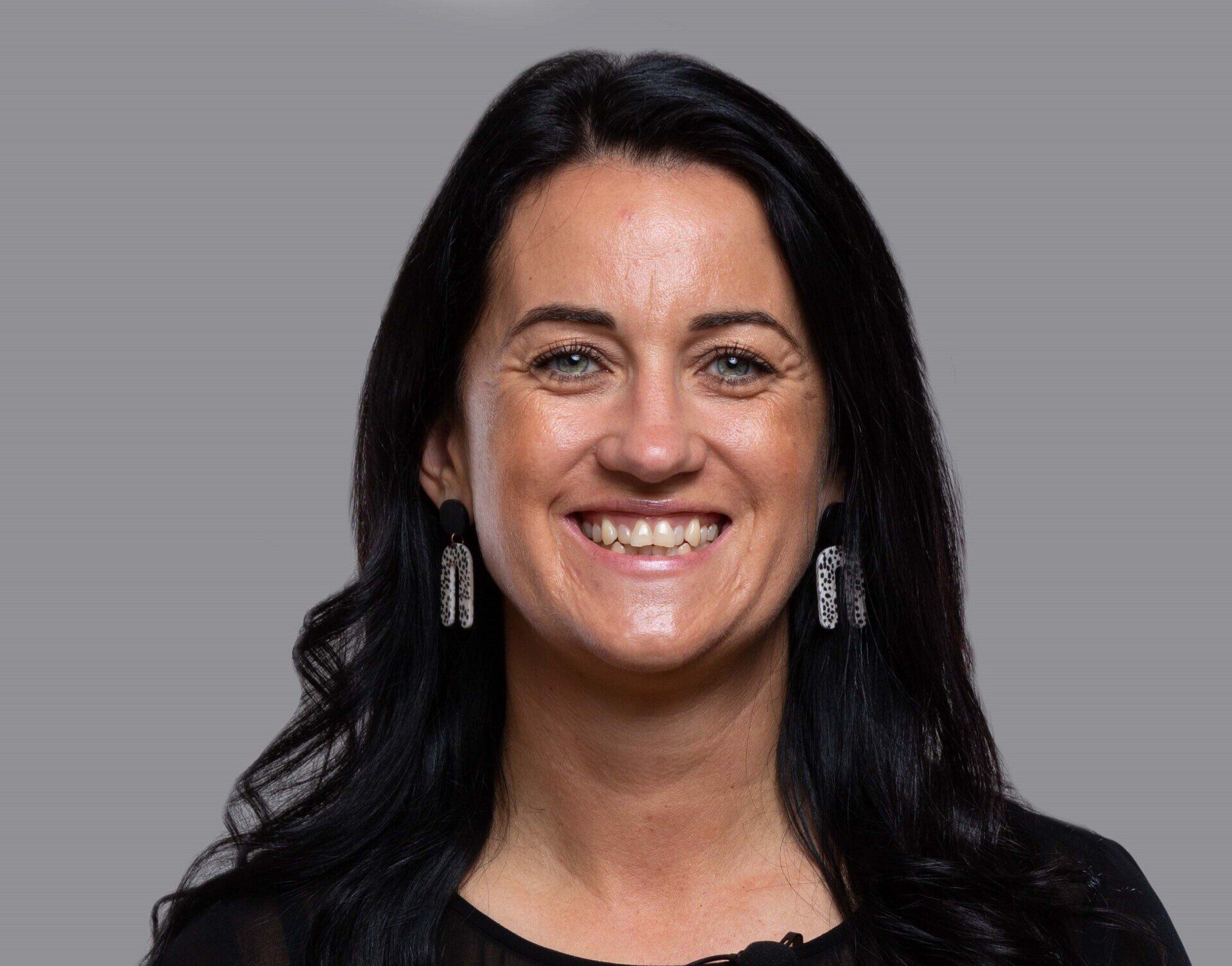 A woman with long black hair and earrings is smiling for the camera.