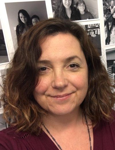 A woman is smiling in front of a wall of pictures