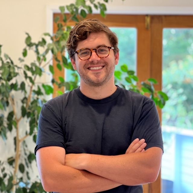 A man wearing glasses and a black shirt is smiling with his arms crossed