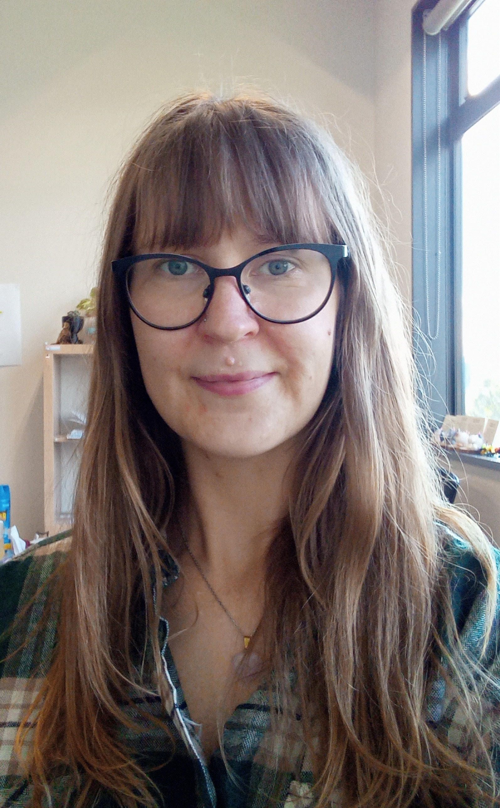 A woman wearing glasses and a plaid shirt is smiling for the camera.