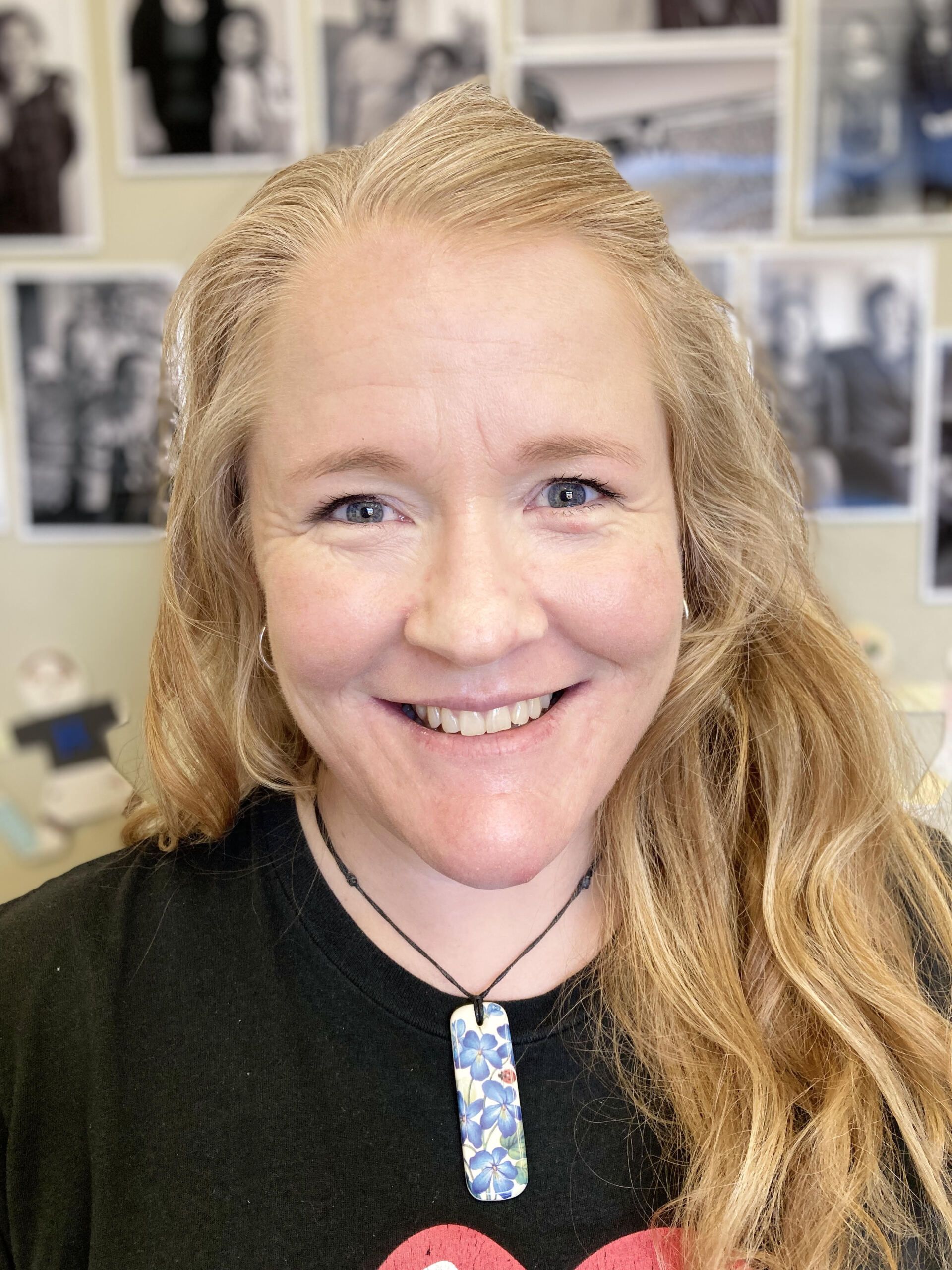 A woman wearing a black shirt and a necklace is smiling.