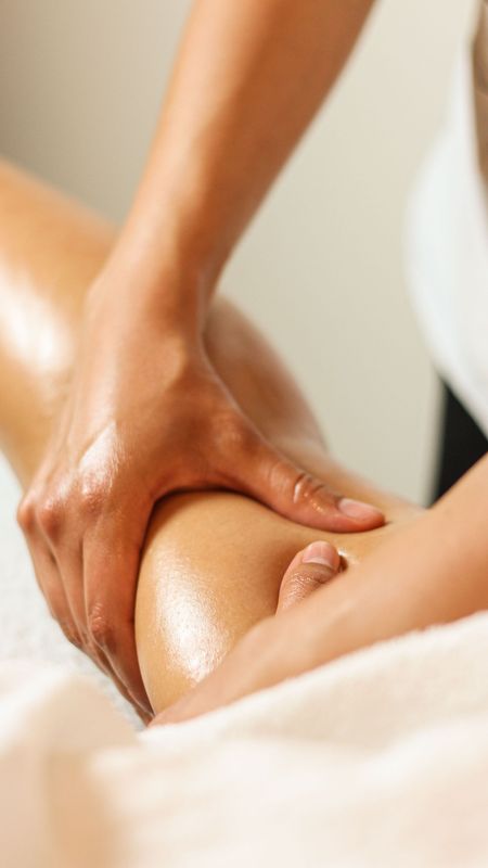Mani che massaggiano la gamba di una persona con dell'olio su un lettino da spa