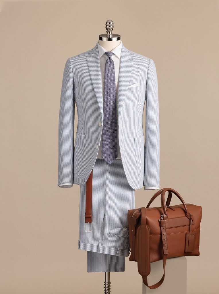 Blue and white striped suit on a mannequin with a brown leather bag, and a belt against a beige backdrop.
