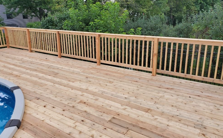 Man using a drill on wooden deck near a house with a saw in the background.