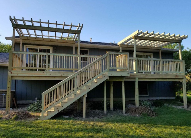 Brick pathway curves through a lush backyard with a deck, trees, and flowers under a sunny sky.
