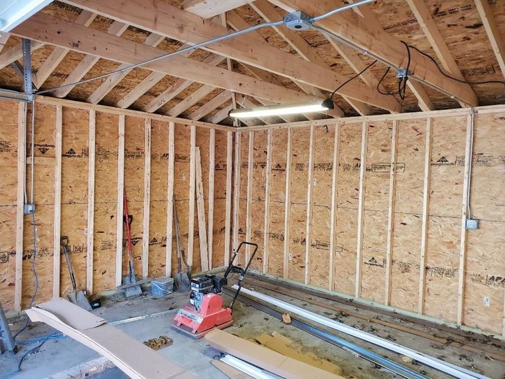 Two people constructing a wooden garage frame in a yard with snow, near a fence and houses.