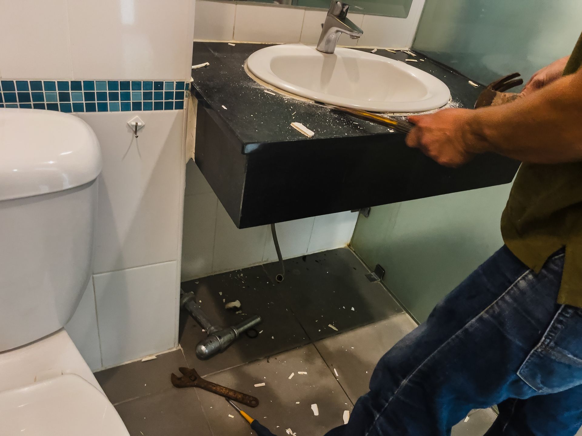 Person removing a bathroom sink from the wall with tools. The sink is white, and the countertop is black.