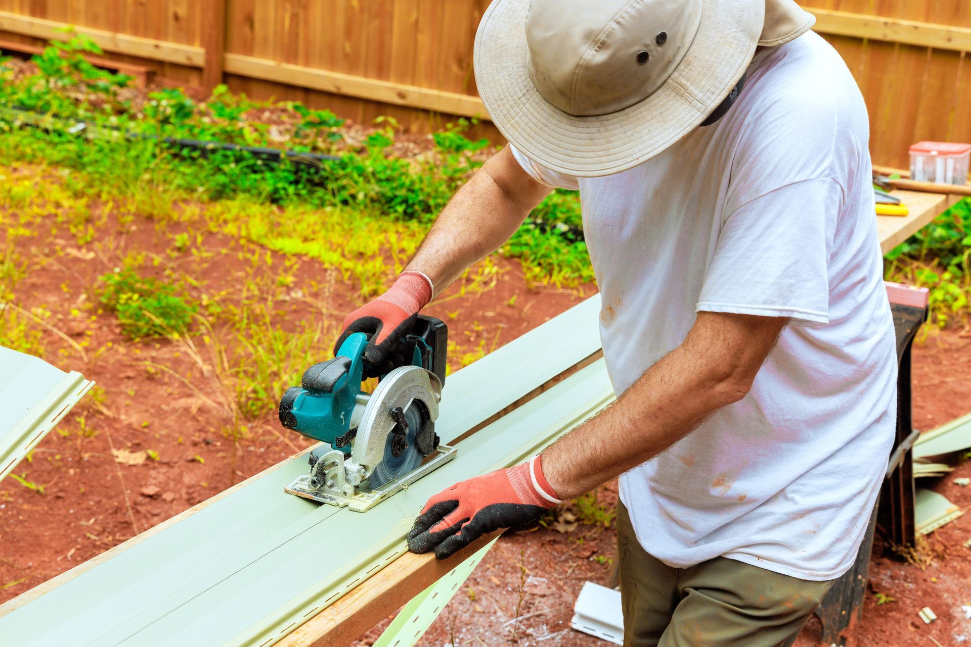 Person in hat using a circular saw to cut wood outdoors.