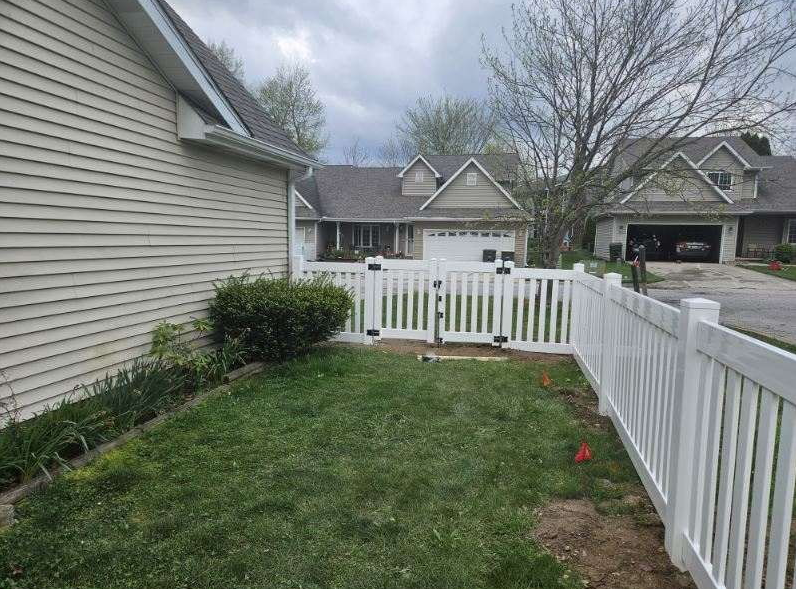 Person using a power drill on a wooden fence outdoors, near a chain link fence.