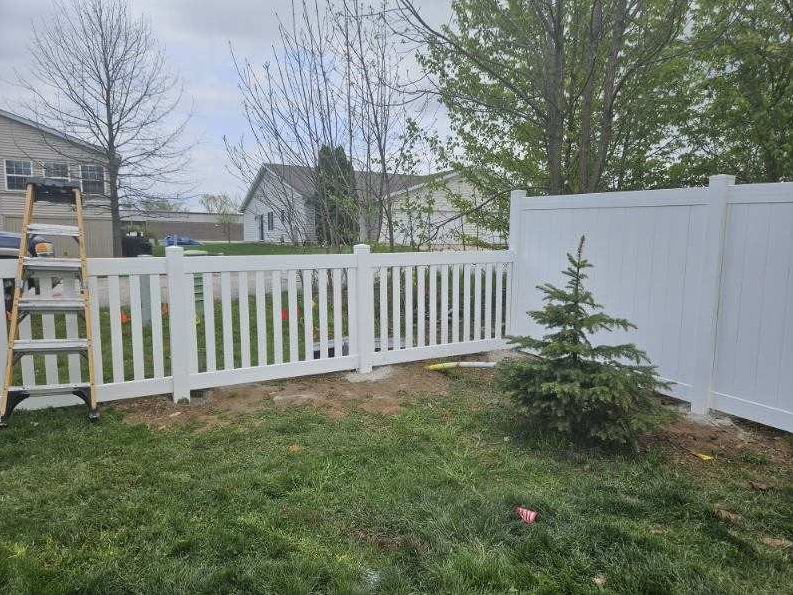 White picket fence with decorative finials along a tree-lined street.