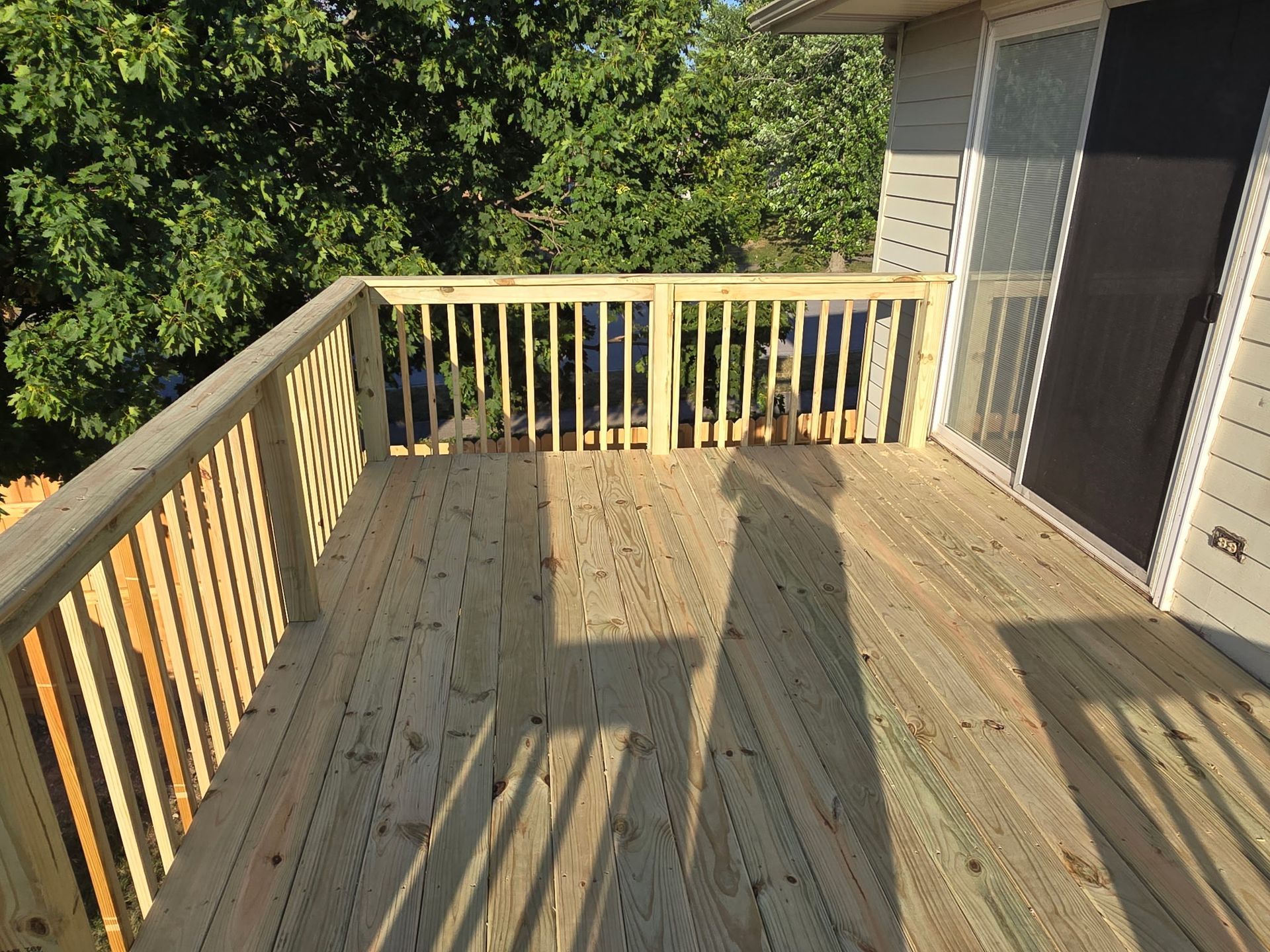 Wooden deck with railings, next to a sliding glass door. Overlooking trees.