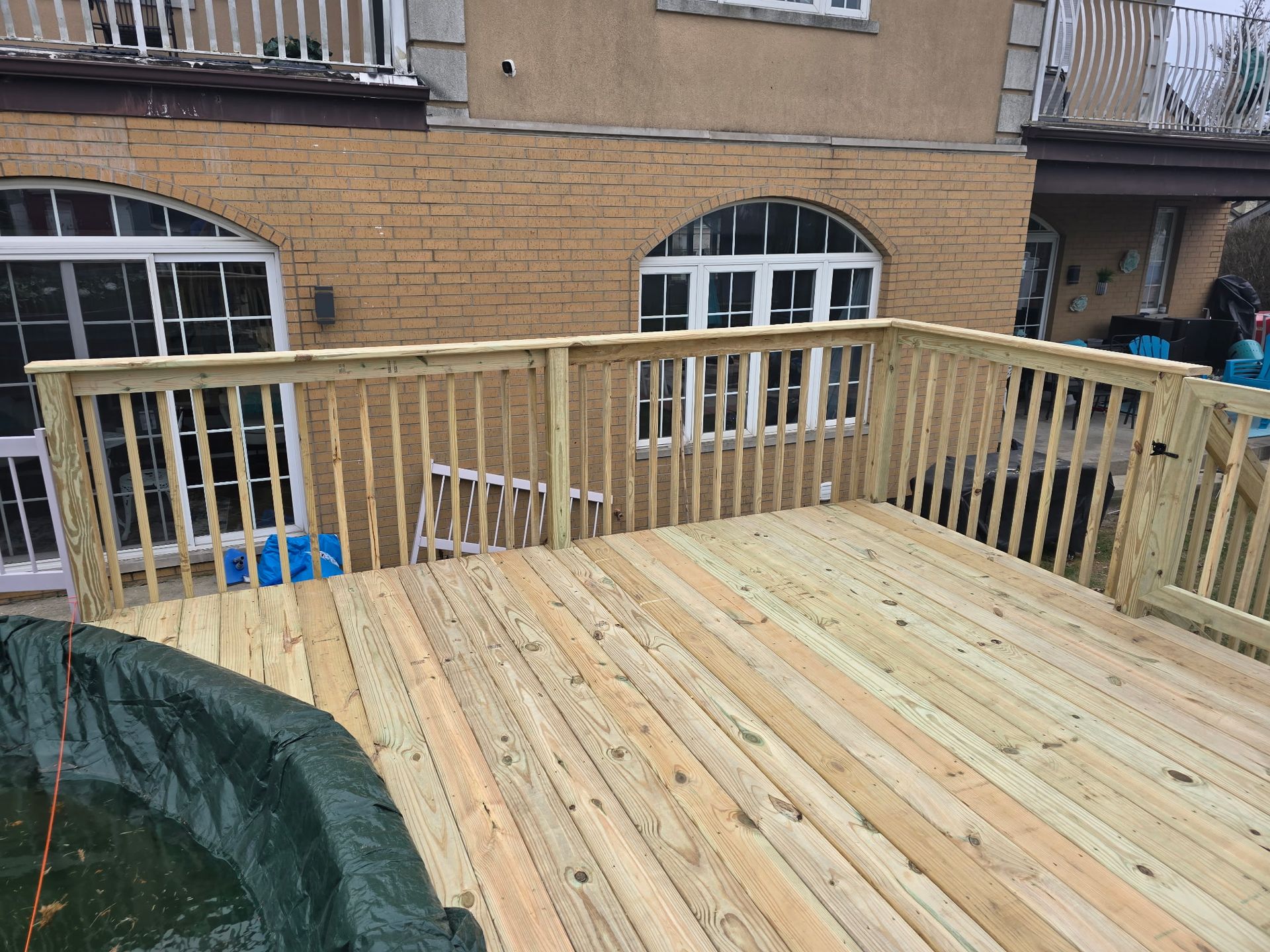 Wooden deck with railing attached to a brick building, near a covered pool.