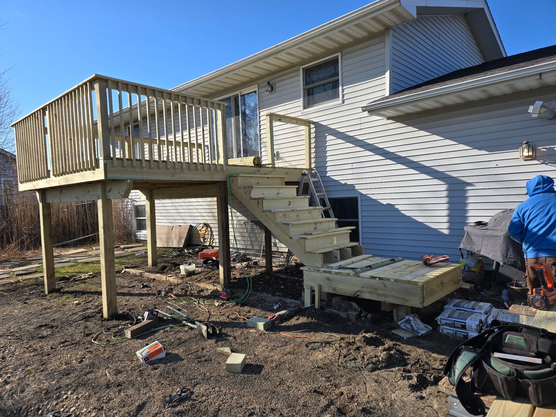 New wooden deck attached to a white house with stairs and a person working on construction.
