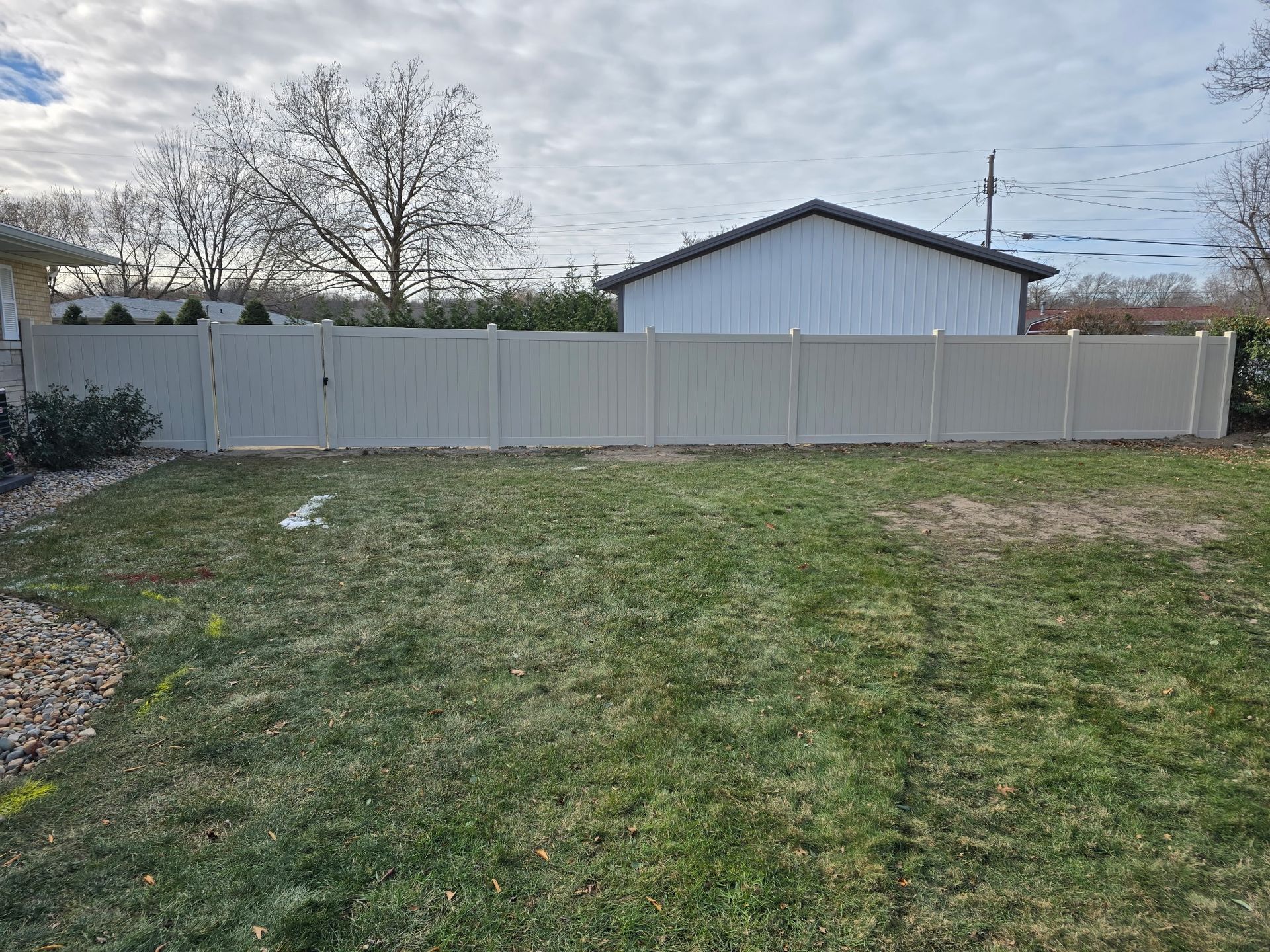 A tan vinyl fence in a backyard, with a lawn in the foreground and a building in the background.