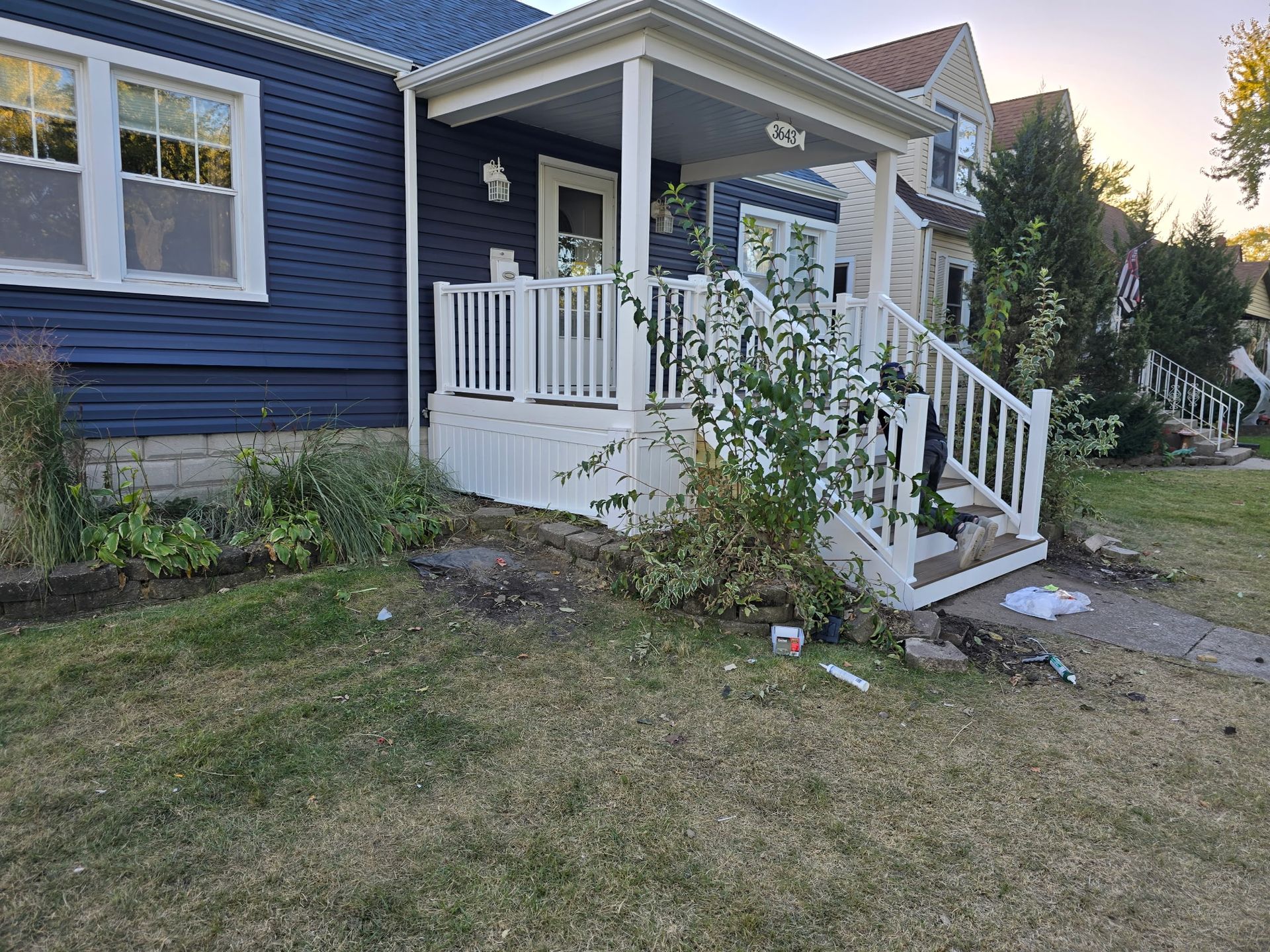 Blue house with white porch and stairs, overgrown landscaping, on a grassy lawn.