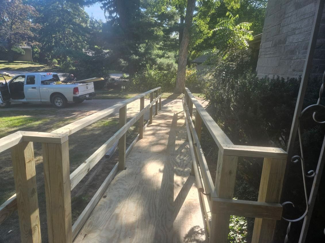 Wooden ramp with handrails leading to an entrance, a white pickup truck is parked on the left.
