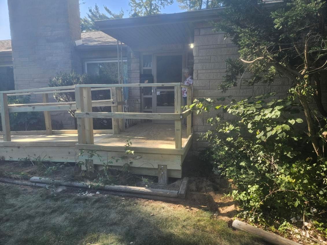 A newly constructed wooden deck with railing at the entrance of a building with brick siding.