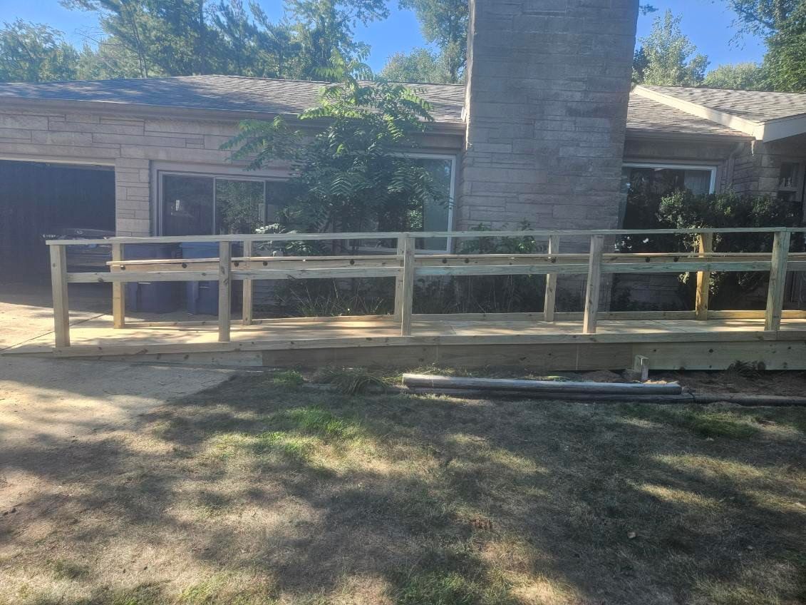 Ramp with wooden railings leads to a house with stone siding and a large chimney.
