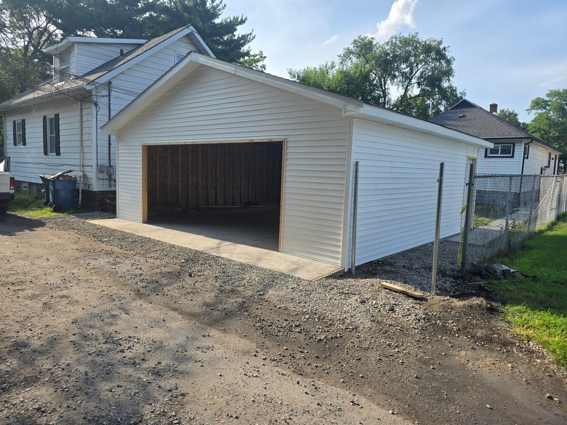 White detached garage with open doorway on gravel driveway, next to a chain-link fence.