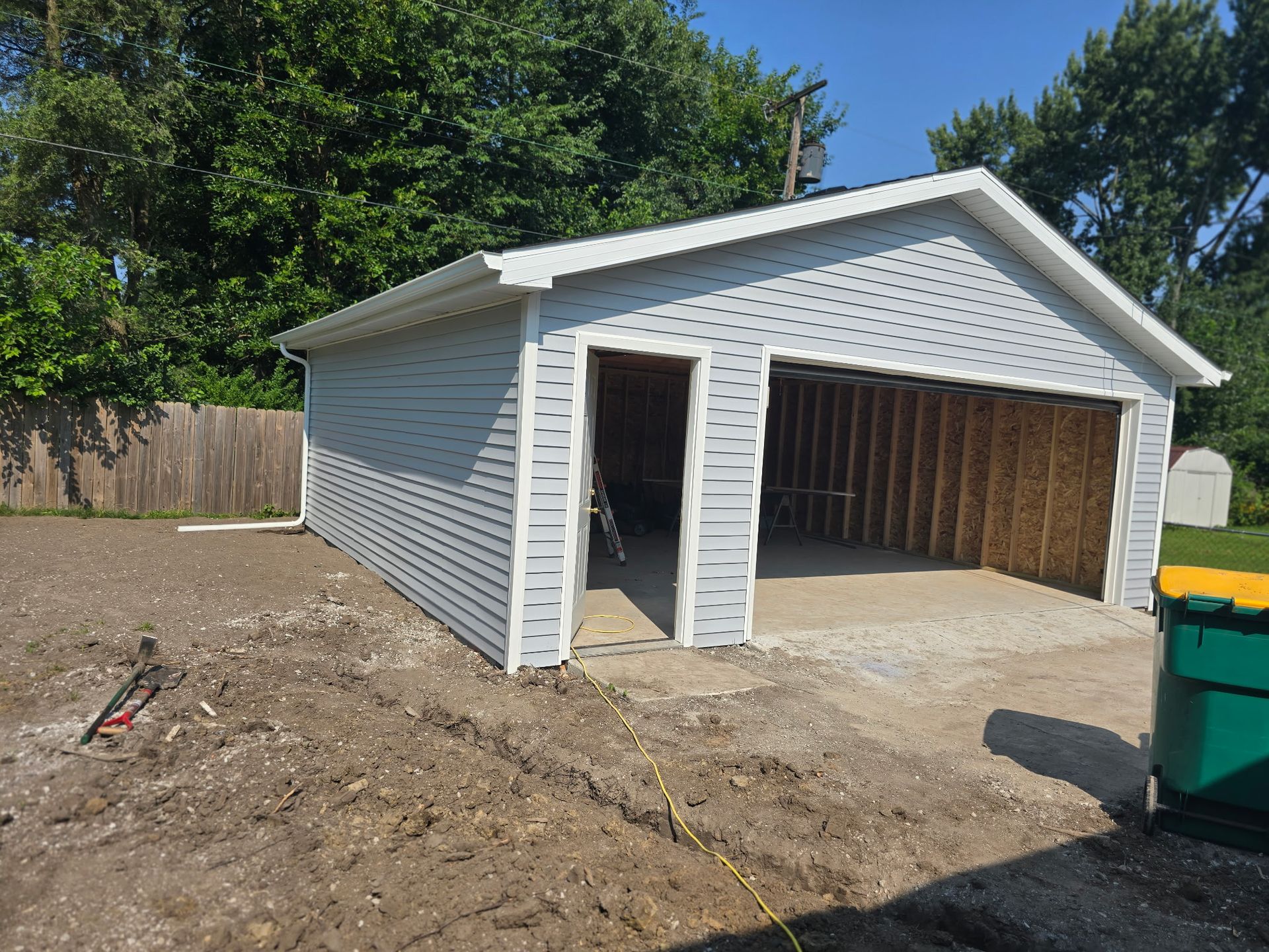 Light blue sided garage with two bays, one open. Concrete driveway. Exterior view.