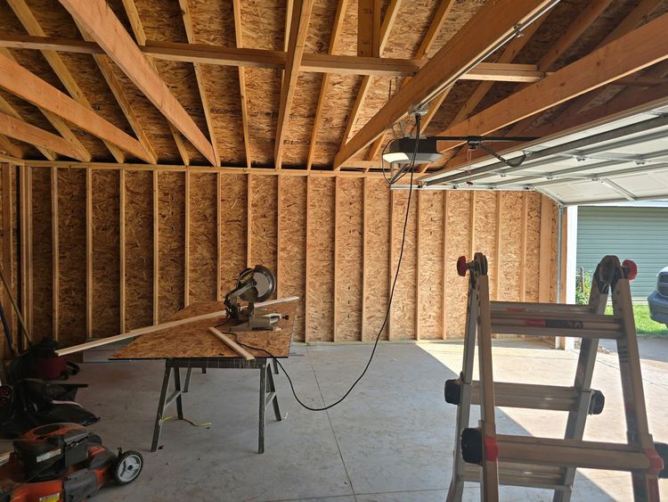 Construction worker in a safety vest and hard hat, looking at blueprints inside a building frame.