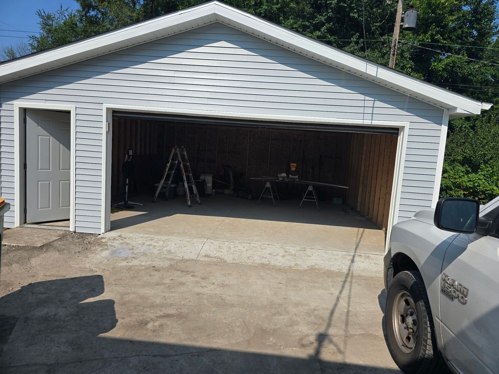 Garage with open door, light blue siding, gray door, and gravel driveway. A white truck is on the right.