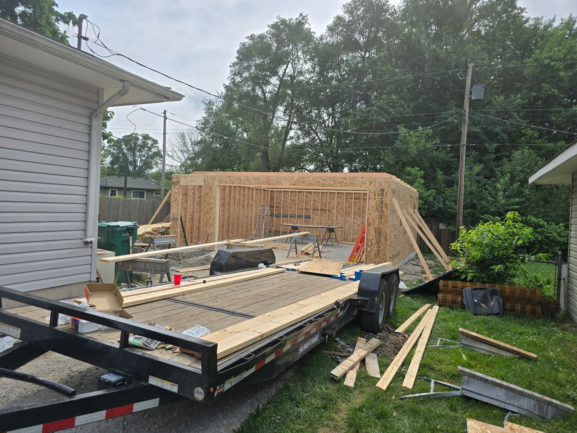 Construction site: a wooden structure under construction, with a trailer loaded with wood in front.