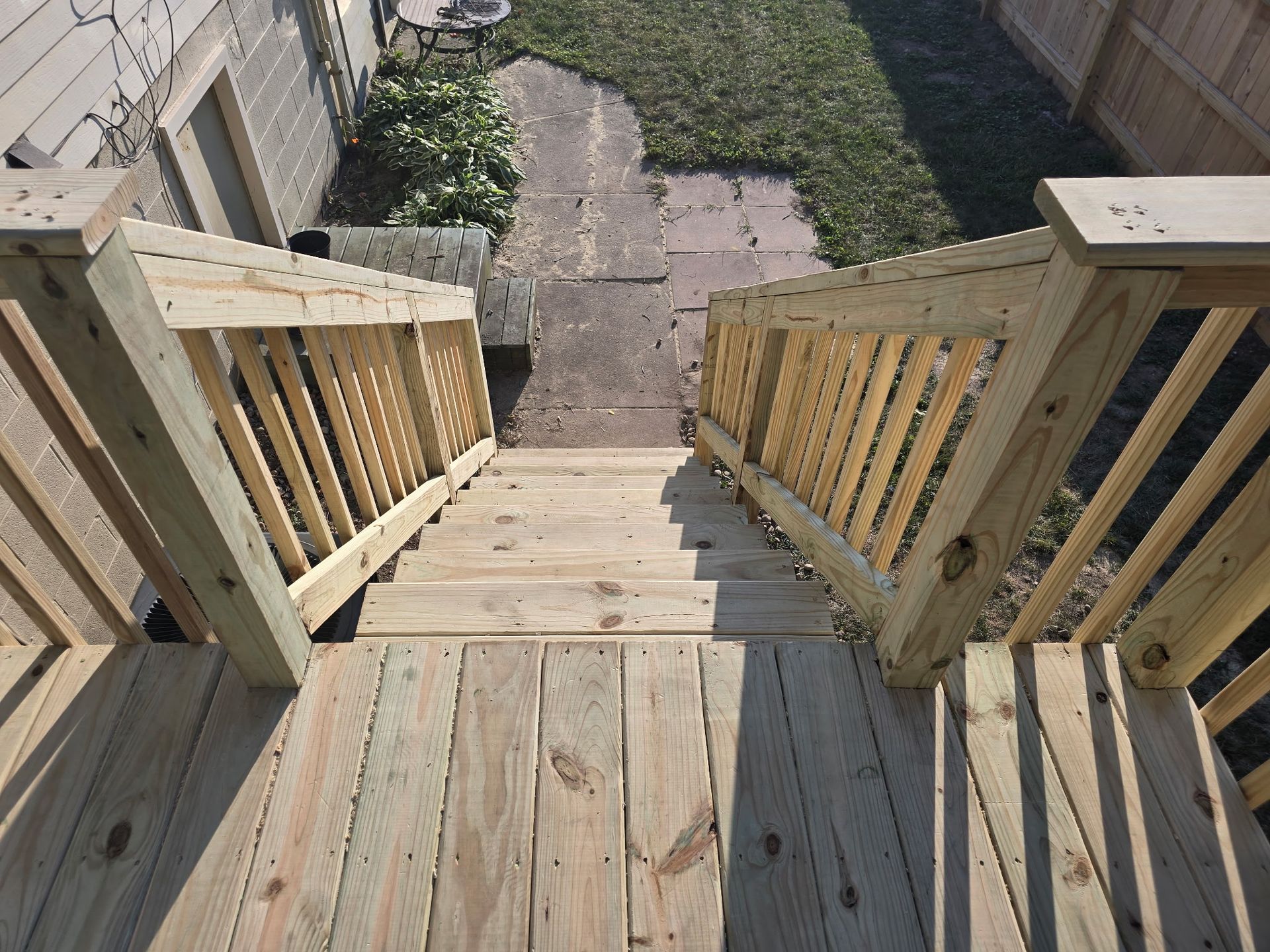 Wooden deck with stairs leading down to a brick pathway and grassy yard.