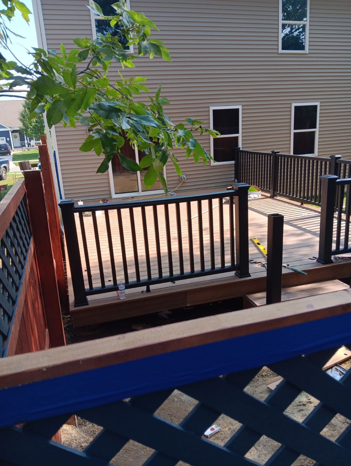 Wooden deck with black railing and brown boards, next to a tan house with windows.